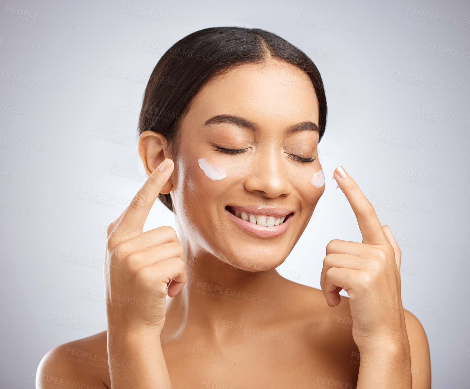 Buy stock photo Studio shot of an attractive young woman applying moisturiser to her face against a grey background