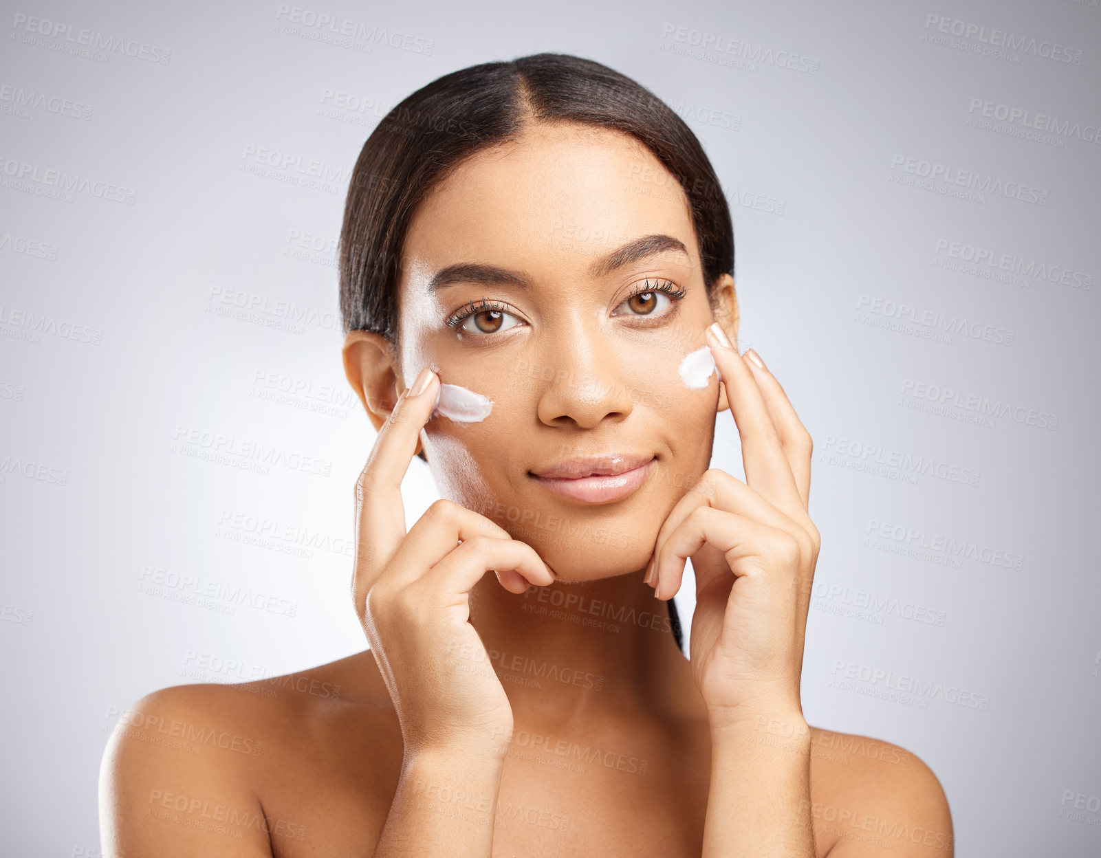 Buy stock photo Studio shot of an attractive young woman applying moisturiser to her face against a grey background