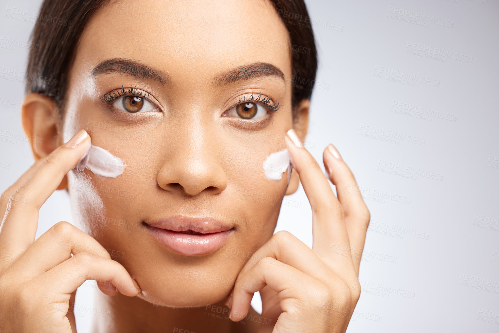 Buy stock photo Studio shot of an attractive young woman applying moisturiser to her face against a grey background