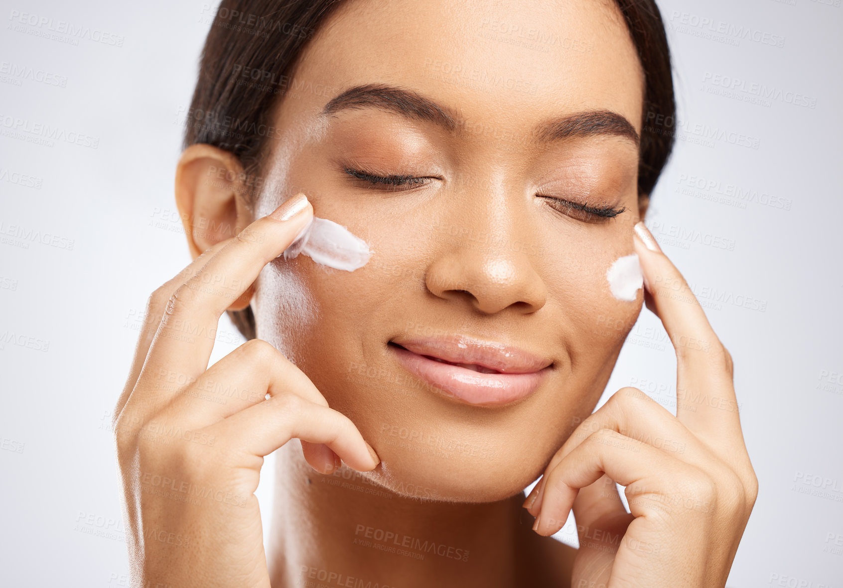 Buy stock photo Studio shot of an attractive young woman applying moisturiser to her face against a grey background