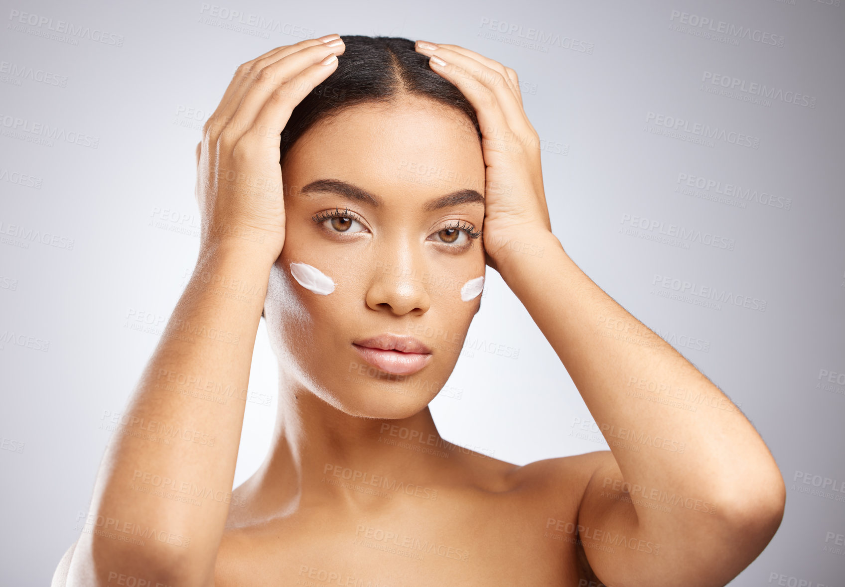 Buy stock photo Studio shot of an attractive young woman applying moisturiser to her face against a grey background