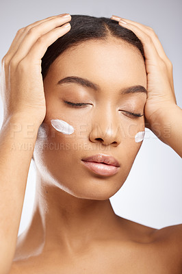 Buy stock photo Studio shot of an attractive young woman applying moisturiser to her face against a grey background