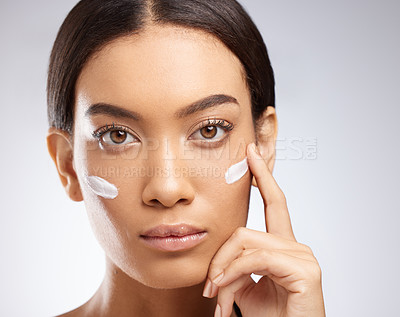 Buy stock photo Studio shot of an attractive young woman applying moisturiser to her face against a grey background