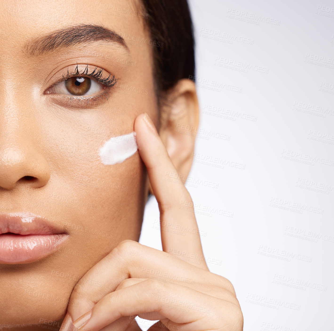 Buy stock photo Studio shot of an attractive young woman applying moisturiser to her face against a grey background