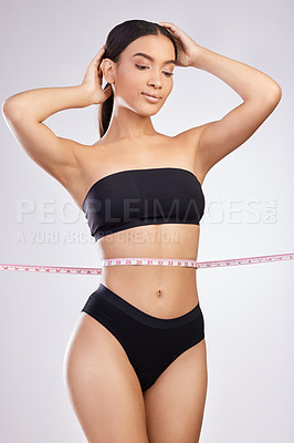 Buy stock photo Studio shot of a beautiful young woman posing with a tape measure around her waist against a white background