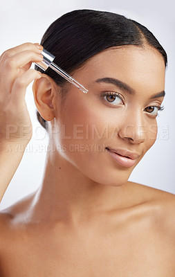 Buy stock photo Studio shot of an attractive young woman using a serum on her face against a grey background