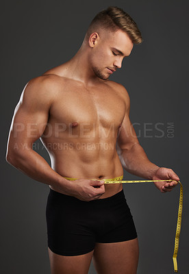 Buy stock photo Cropped shot of a handsome and athletic young man measuring his waist in studio against a dark background