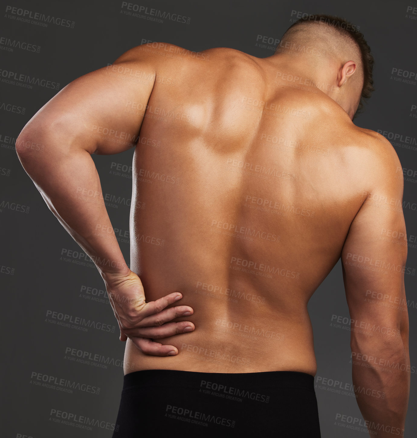 Buy stock photo Cropped shot of an unrecognizable and athletic young man holding his back in pain while shirtless in studio against a dark background