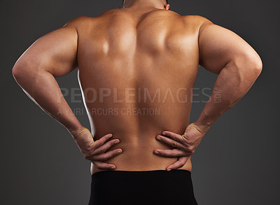 Buy stock photo Cropped shot of an unrecognizable and athletic young man holding his back in pain while shirtless in studio against a dark background