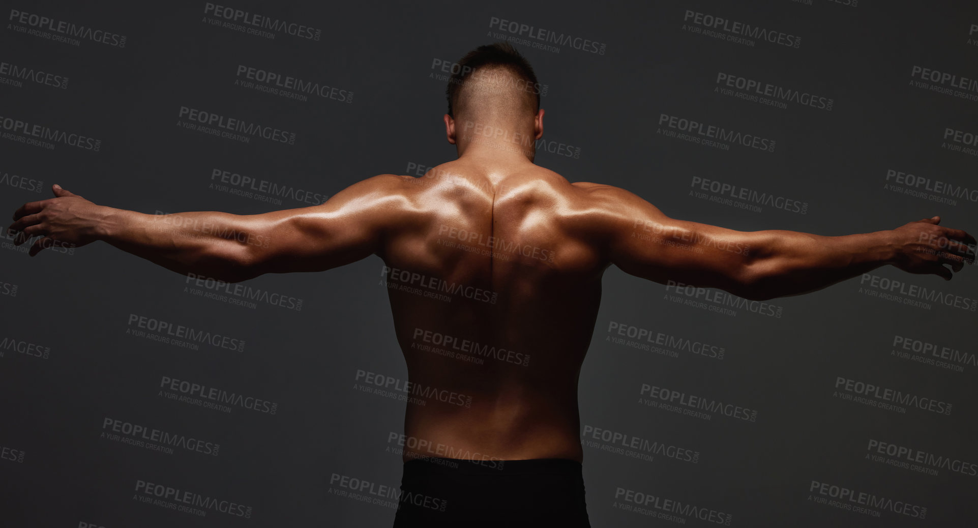 Buy stock photo Rearview shot of an unrecognizable and athletic young man posing shirtless in studio against a dark background