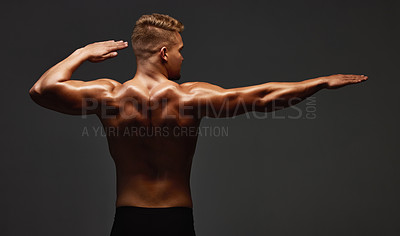 Buy stock photo Rearview shot of a handsome and athletic young man posing shirtless in studio against a dark background