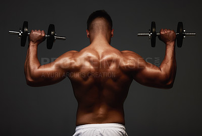 Buy stock photo Rearview shot of an unrecognizable and athletic young man lifting weights while shirtless in studio against a dark background