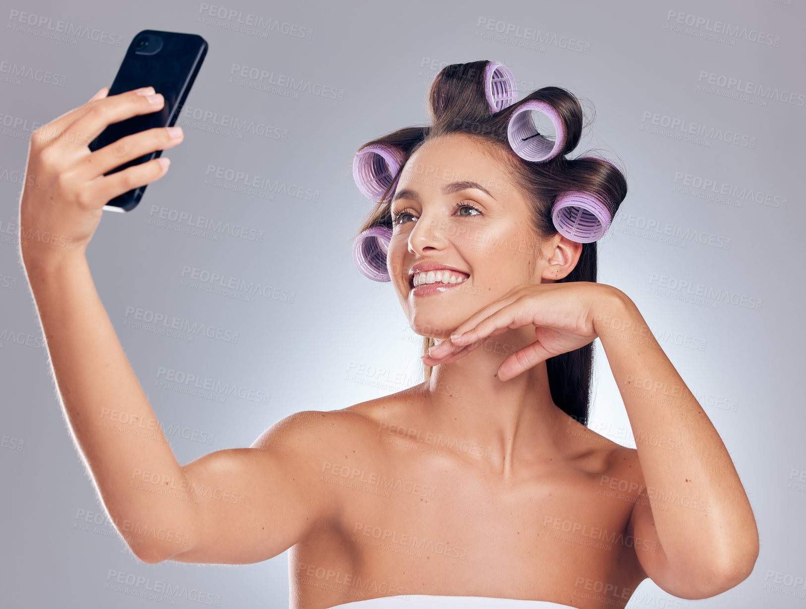 Buy stock photo Hair roller, woman and phone for selfie with transformation results, social media and blog app in studio. Mobile picture, haircare influencer and salon tools for curling hairstyle by grey background