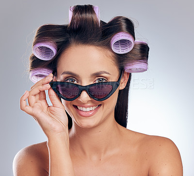 Buy stock photo Shot of an attractive young woman standing alone in the studio with rollers in her hair and posing with sunglasses