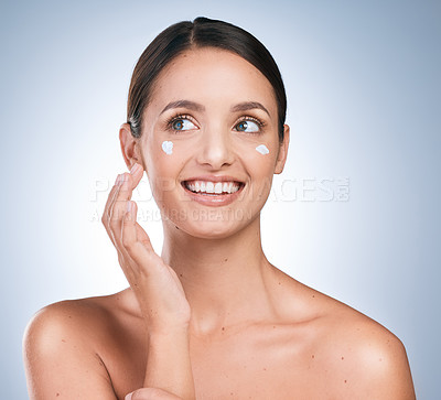 Buy stock photo Shot of an attractive young woman applying moisturiser against a blue background