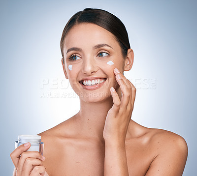 Buy stock photo Shot of an attractive young woman applying moisturiser against a blue background