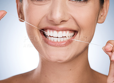 Buy stock photo Closeup cropped shot of a young woman flossing her teeth against a blue background