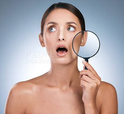 Buy stock photo Shot of a young woman using a magnifying glass to check her skin against a blue background