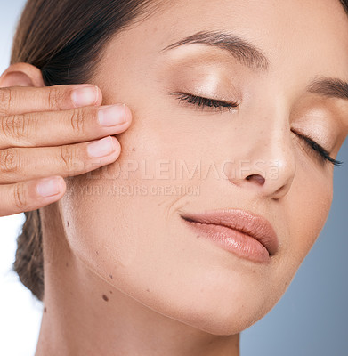 Buy stock photo Headshot of a beautiful woman massaging product into her face against a blue background