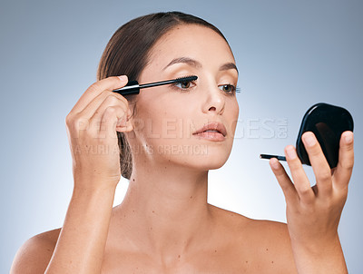 Buy stock photo Shot of a young attractive woman applying makeup against a blue background