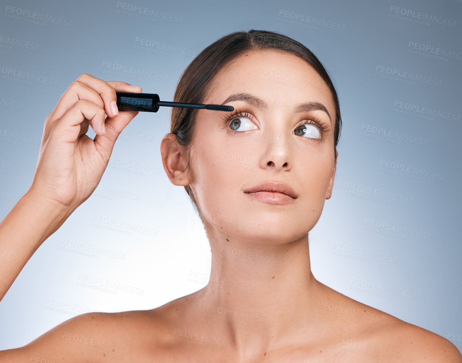Buy stock photo Shot of a young attractive woman applying makeup against a blue background
