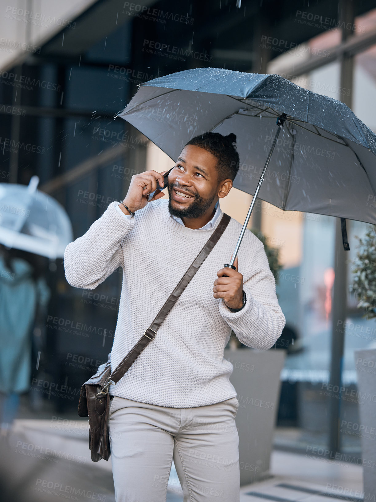 Buy stock photo Cropped shot of a handsome young businessman making a phonecall while walking through the city with an umbrella