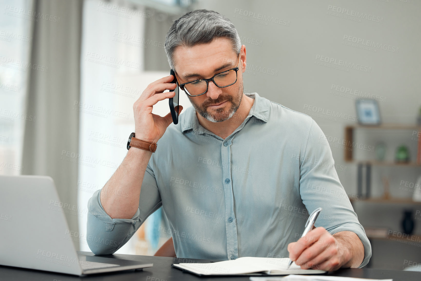 Buy stock photo Cropped shot of a handsome mature man making a phonecall while working on his finances at a desk at home