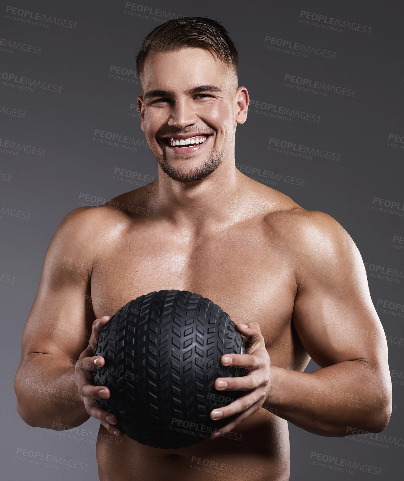 Buy stock photo Shot of a sporty young man holding an exercise ball while standing against a grey background