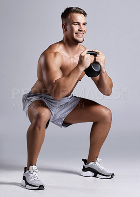Buy stock photo Shot of a sporty young man working out with a kettle bell against a grey background