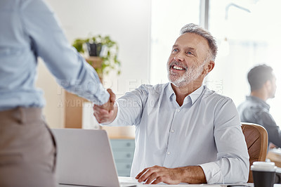 Buy stock photo Shot of a mature businessman shaking hands with his colleague in a modern office