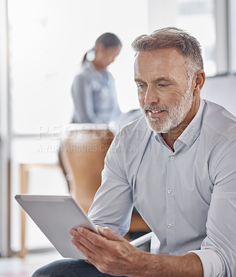 Buy stock photo Shot of a mature businessman using a digital tablet in a modern office