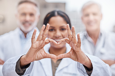 Buy stock photo Shot of a young female doctor making a heart shape with her hands while standing in the city