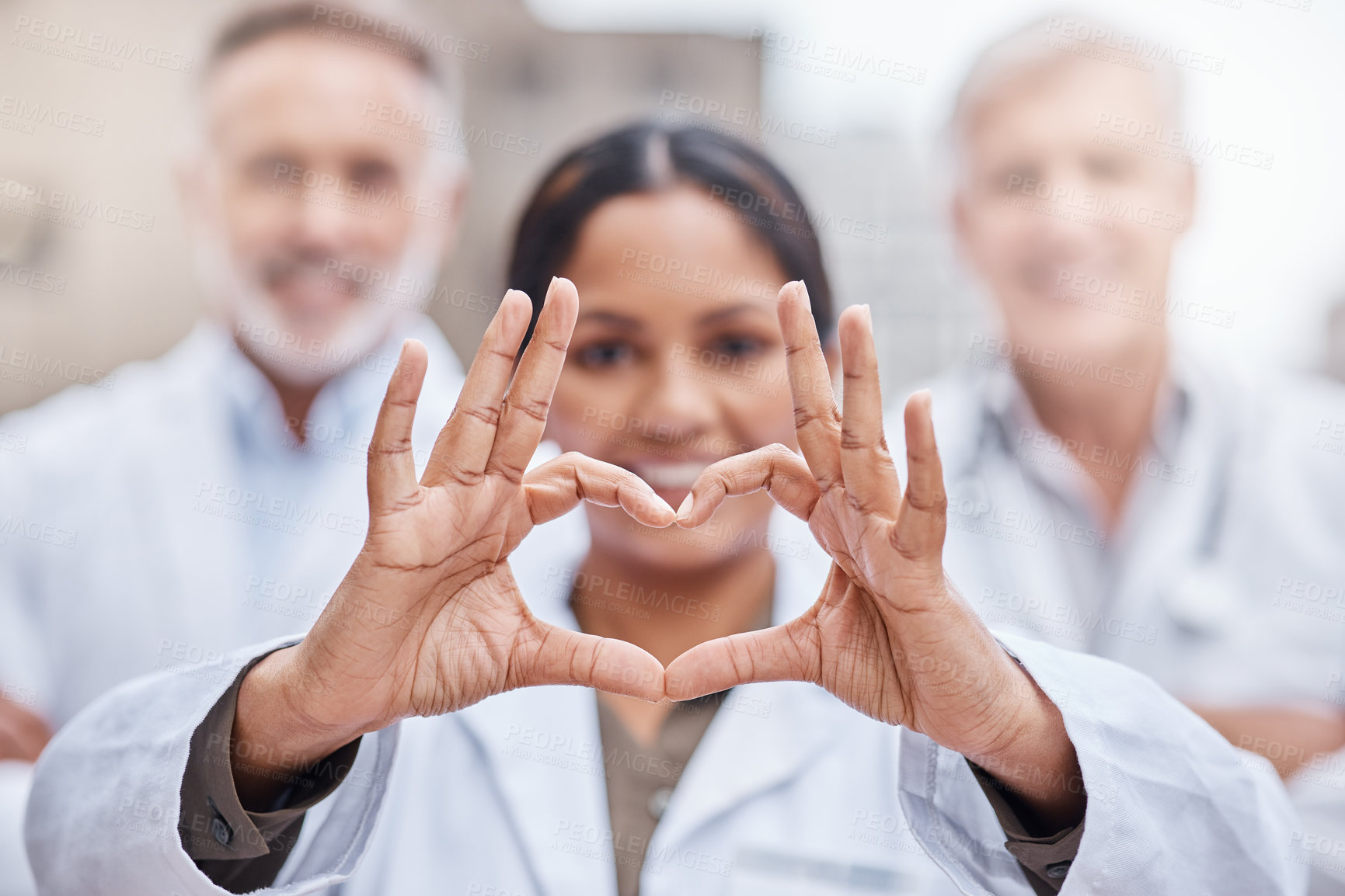 Buy stock photo Shot of a young female doctor making a heart shape with her hands while standing in the city