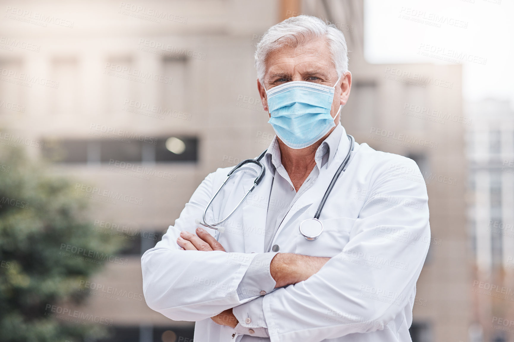 Buy stock photo Shot of a mature male doctor standing with his arms crossed in the city