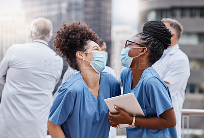 Buy stock photo Shot of two young female doctors using a digital tablet in the city