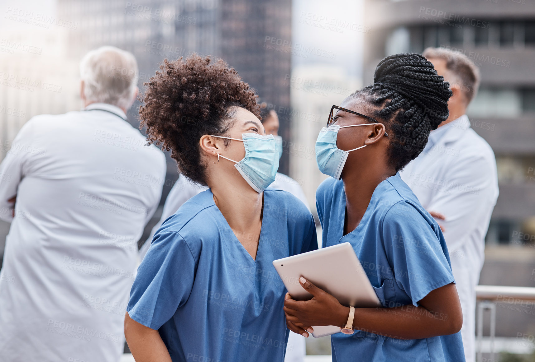 Buy stock photo Shot of two young female doctors using a digital tablet in the city