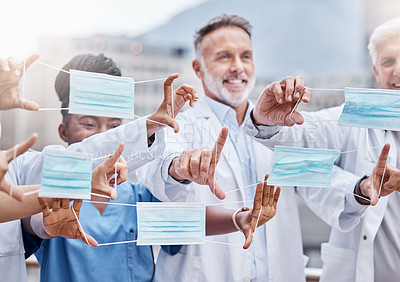 Buy stock photo Shot of a group of doctors holding up masks in the city