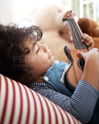 Buy stock photo Shot of an adorable young boy playing with a guitar in his bedroom at home