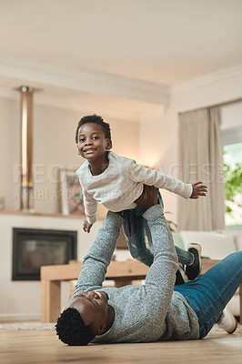 Buy stock photo Cropped shot of a handsome young man lifting is son high up in the air while playing on the living room floor at home