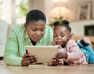 Buy stock photo Full length shot of an attractive young woman and her daughter using a tablet while lying on the living room floor at home