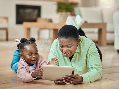 Buy stock photo Full length shot of an attractive young woman and her daughter using a tablet while lying on the living room floor at home