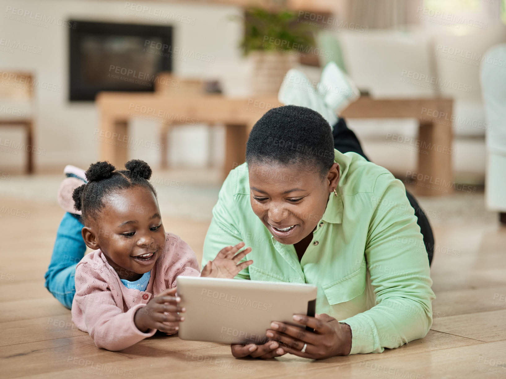 Buy stock photo Full length shot of an attractive young woman and her daughter using a tablet while lying on the living room floor at home