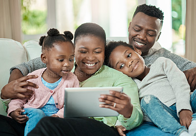 Buy stock photo Cropped shot of an affectionate young family of four using a tablet while sitting on a sofa in their living room at home