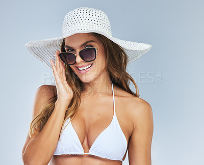 Buy stock photo Studio portrait of an attractive young woman wearing sunglasses while posing in a bikini and sunhat against a grey background