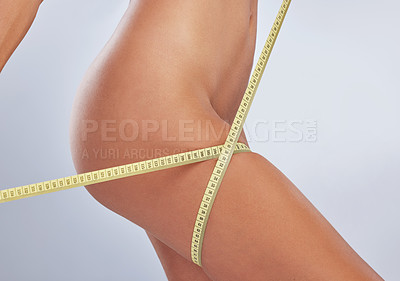 Buy stock photo Cropped shot of an unrecognizable woman standing alone in the studio and using a tape measure to measure her thigh