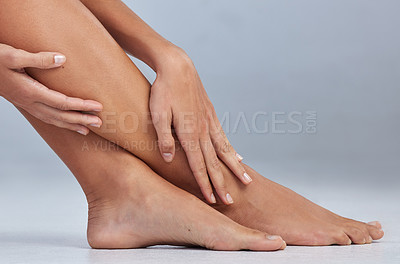 Buy stock photo Cropped shot of an unrecognizable woman sitting alone and touching her legs in the studio
