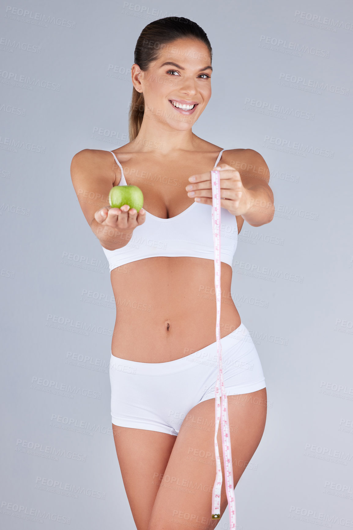 Buy stock photo Studio portrait of an attractive young woman holding an apple and a measuring tape against a grey background