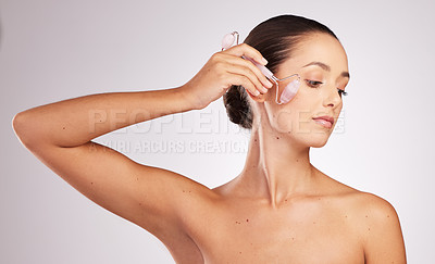 Buy stock photo Shot of an attractive young woman using a jade roller on her face against a studio background