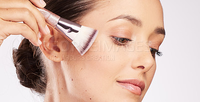 Buy stock photo Shot of an attractive young woman using a makeup brush against a studio background