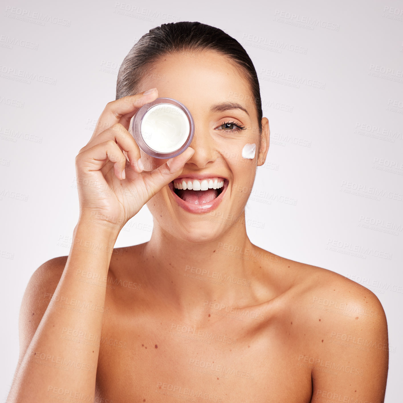 Buy stock photo Shot of an attractive young woman applying moisturiser to her face against a studio background